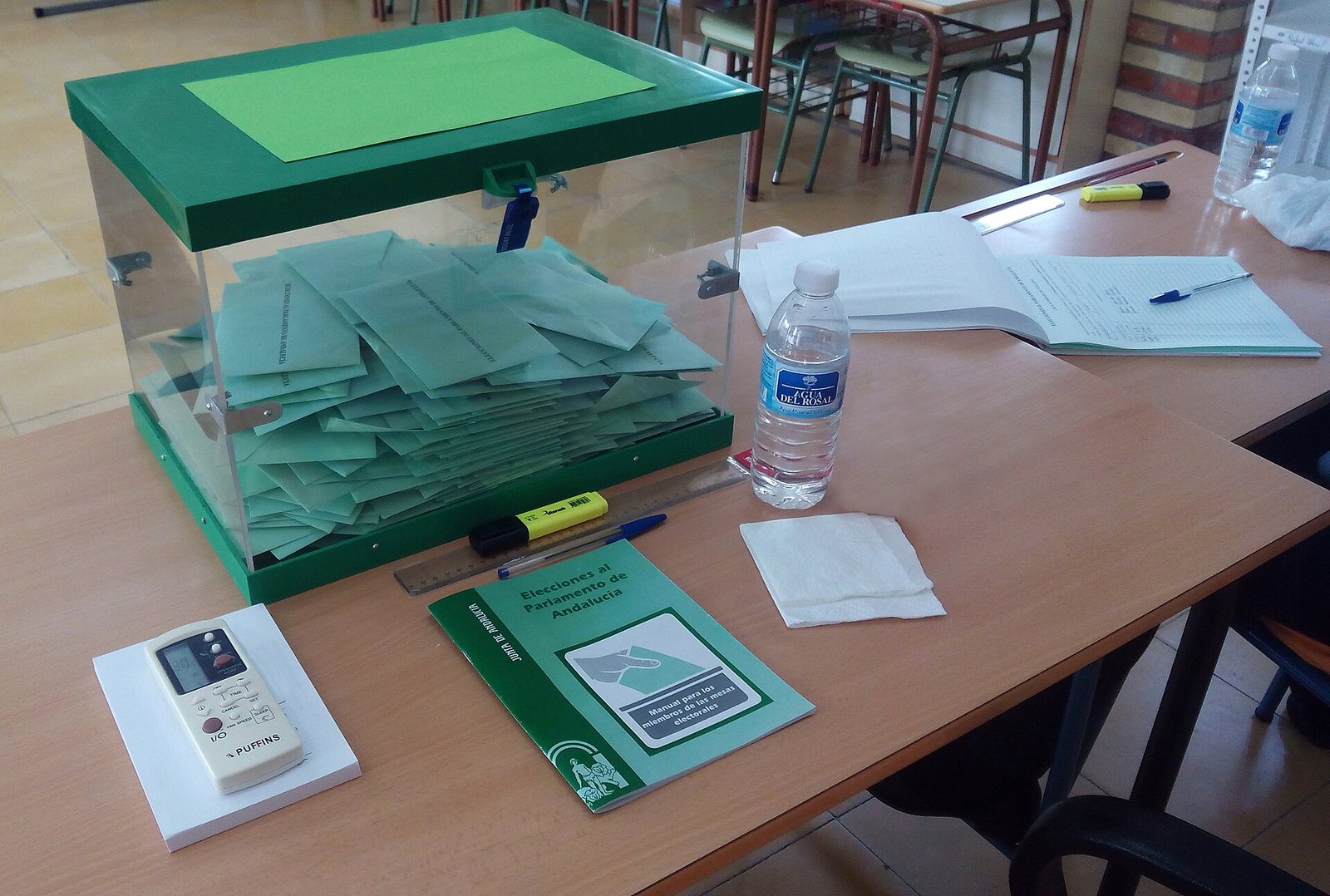Urna de una mesa electoral llena de sobres, con el manual de los miembros de mesa al lado
