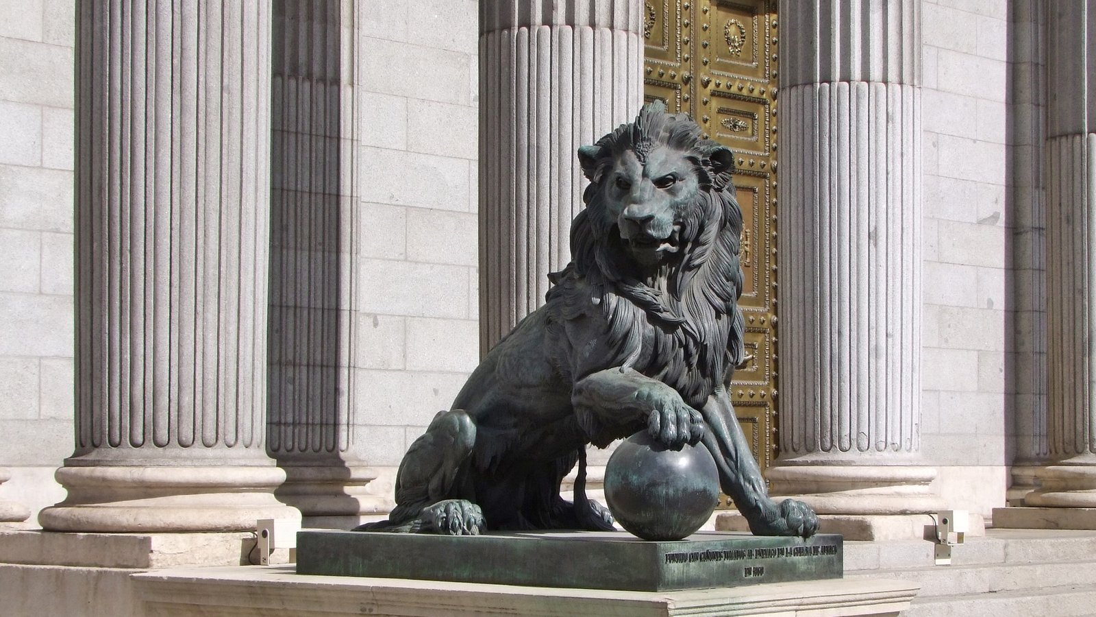 León de bronce con una garra sobre una bola, delante de las columnas de la entrada principal del Congreso de los Diputados
