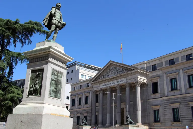 Fachada del Congreso de los Diputados con su frontón y sus columnas, y a la izquierda la estatua de Cervantes sobre su pedestal