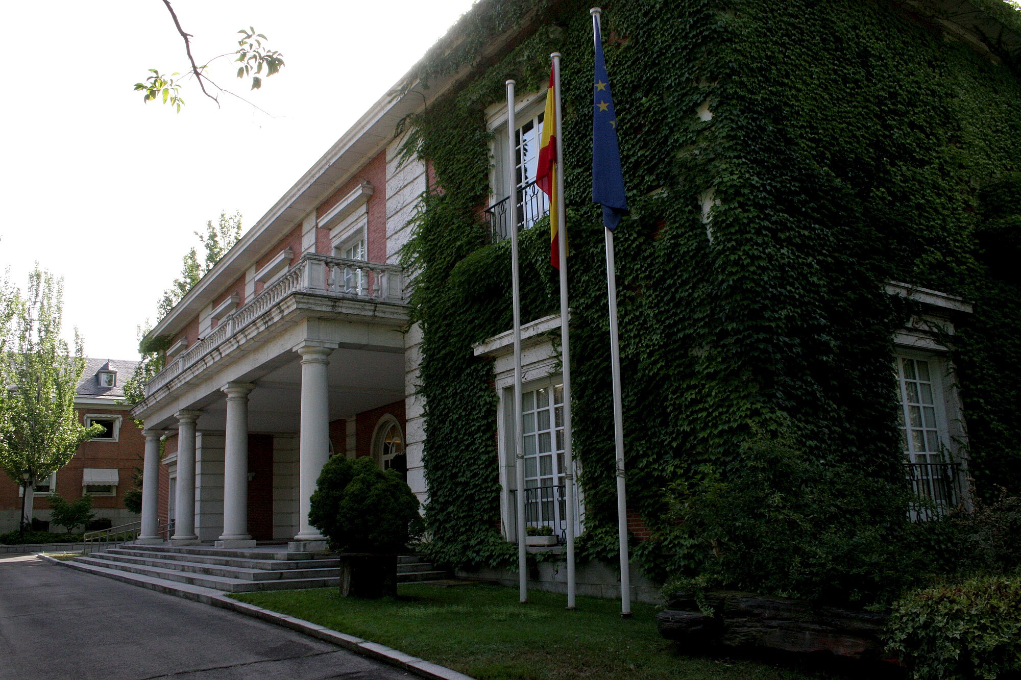 Entrada con columnas del edificio del Consejo de Ministros, en el complejo de la Moncloa, con la fachada cubierta de hiedra y las banderas de España y de la Unión Europea