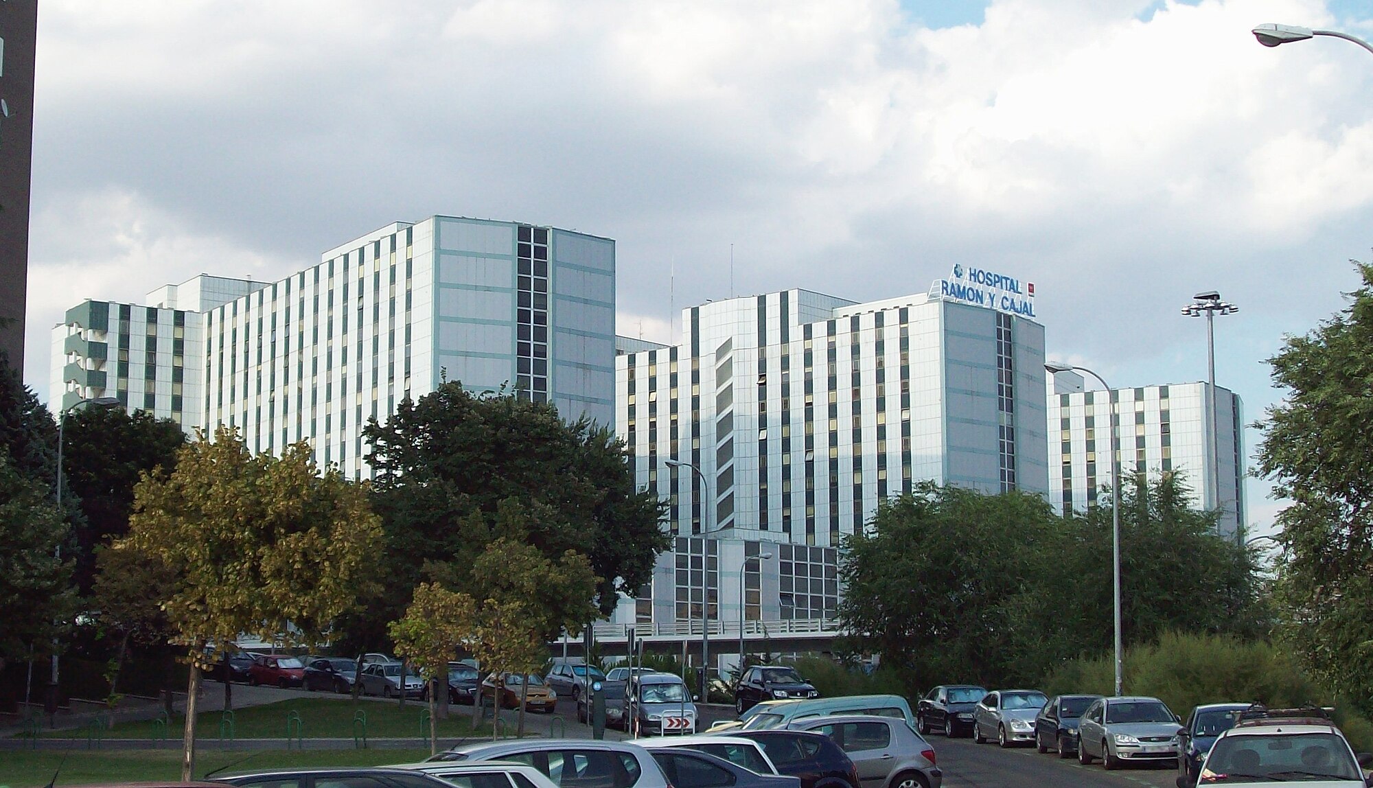 Edificios del Hospital Universitario Ramón y Cajal de Madrid vistos desde lejos, con árboles y un aparcamiento delante