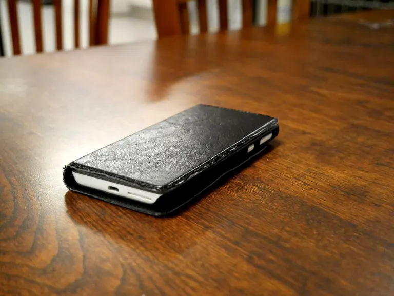 Teléfono móvil dentro de una funda de cuero negra, cerrada, sobre una mesa de madera