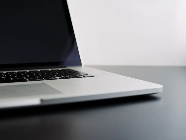 Primer plano del teclado y el borde de un ordenador portátil plateado abierto sobre una mesa oscura