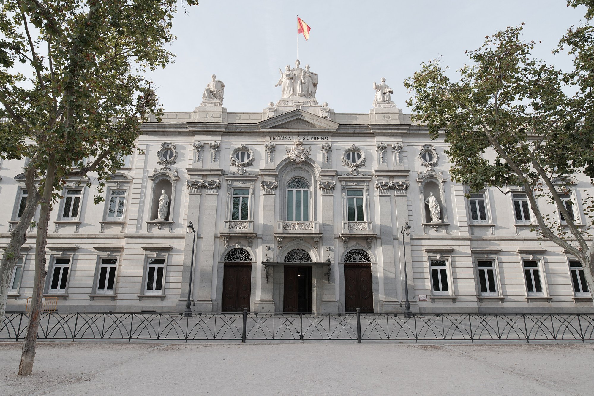 Fachada del Palacio de Justicia de Madrid, sede del Tribunal Supremo, con árboles delante y la bandera de España en lo alto
